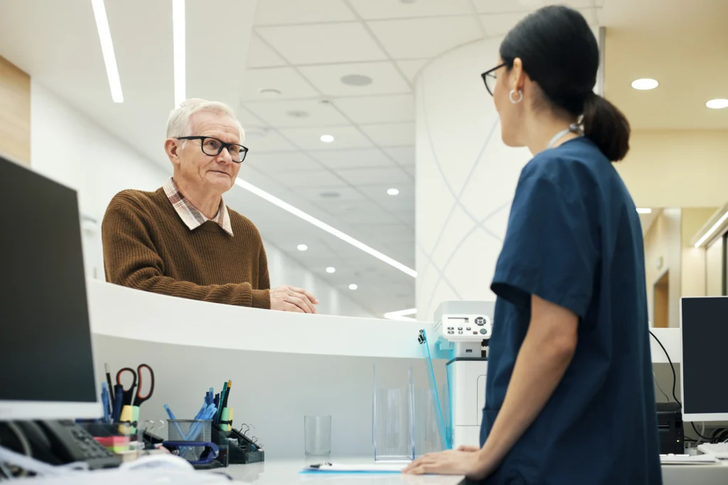 A man using his medicare card at a front desk of a hospital.