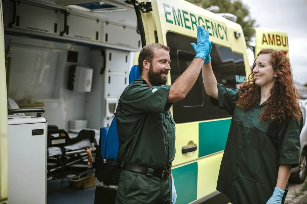 2 healthcare officials giving high five infront of a ambulance.